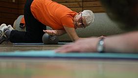 Die 80 jährige Rosi liegt auf dem Boden und schiebt ihren rechten Arm unter dem Bauch durch zum dehnen